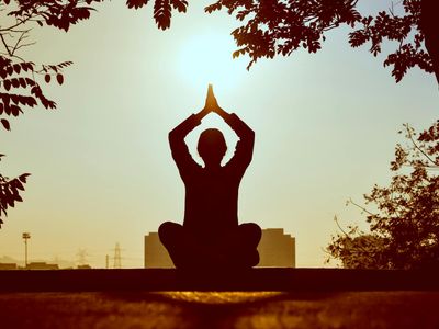 Person meditating peacefully outdoors during sunrise.